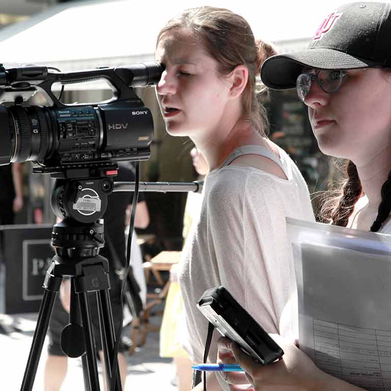Two students practice motion picture production using a video camera and script.