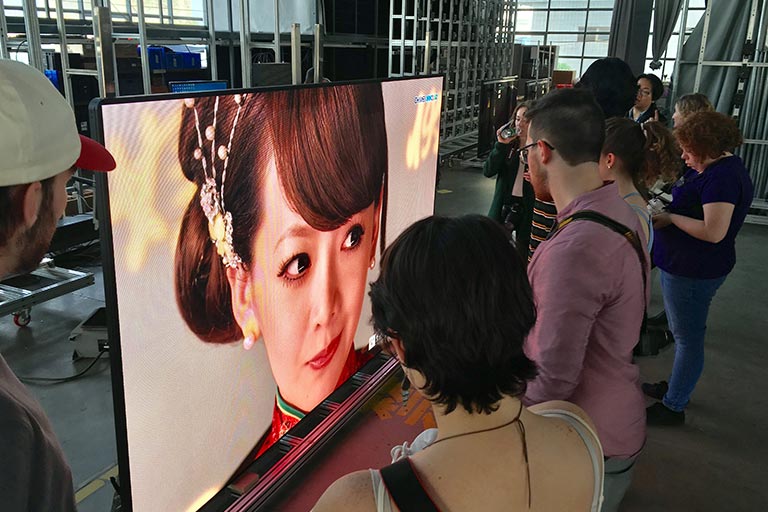 People stand around a screen showing a woman in Chinese traditional dress during a student show.