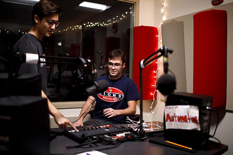 Two students work with sound equipment in a production studio space.