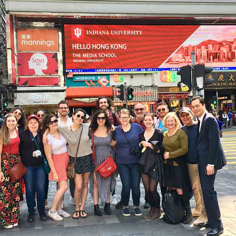 A group of students in front of a sign for The Media School in Hong Kong