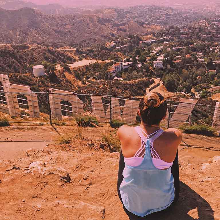 A woman sits on the hillside looking down over the Hollywood sign in Los Angeles.